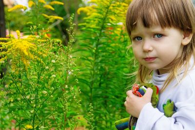 Portrait of cute toddler holding stuffed frog toy by plants