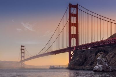 Suspension bridge over river during sunset