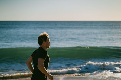 Boy standing on beach against clear sky