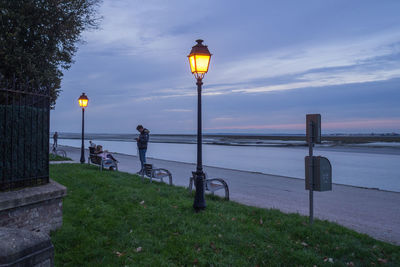 Street light by sea against sky at dusk