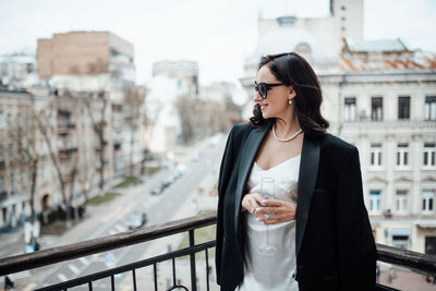 Young woman wearing sunglasses standing on railing in city