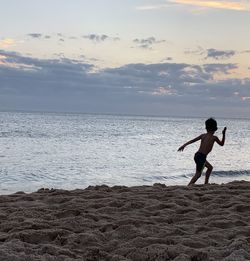 Boy on beach against sky during sunset