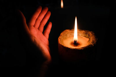 Close-up of hand shielding lit diya in darkroom