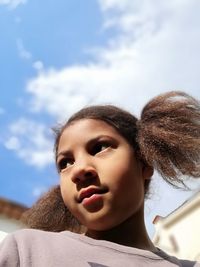 Low angle portrait of young woman looking away against sky