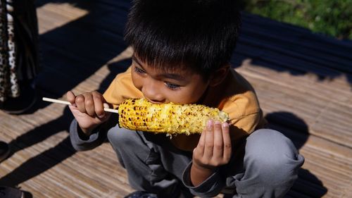 High angle view of boy eating corn while crouching on floor