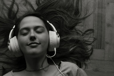 Close-up of woman listening music while lying on hardwood floor