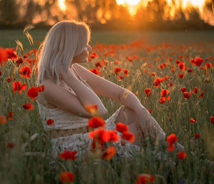 Rear view of woman with red poppy flowers on field