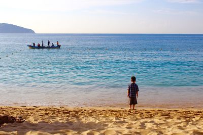 Rear view of boy standing at beach against sky