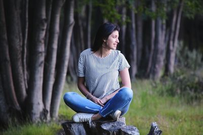 Full length of woman sitting on tree stump in forest