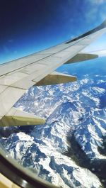 Close-up of airplane wing over landscape against blue sky