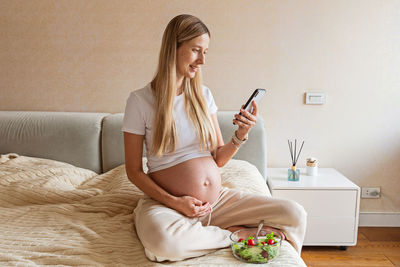 Young woman using mobile phone while sitting on bed at home