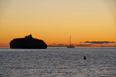 Silhouette rocks by sea against sky during sunset