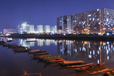 Illuminated buildings by lake against sky in city at night