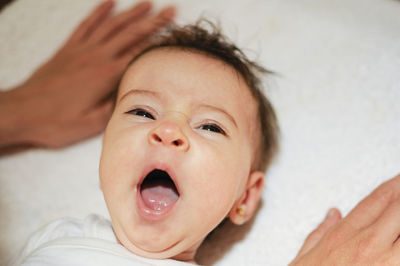 Close-up of cute baby girl yawning while lying on bed at home