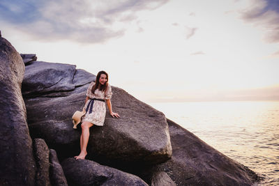 Young woman on rock at beach against sky