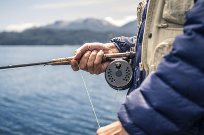 Midsection of man holding fishing rod by sea