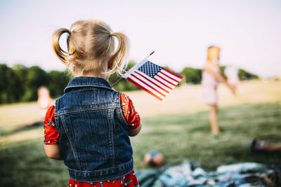 Rear view of girl with small american flag standing on field at park