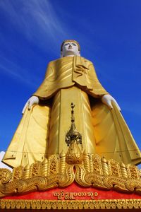 Low angle view of statue against temple building against blue sky