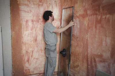 Caucasian man rests a window pane against a wall in a room.