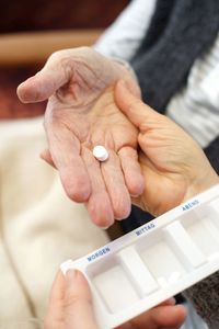 Cropped image of caregiver giving pill with senior woman