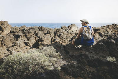 Rear view of woman sitting on rock at beach