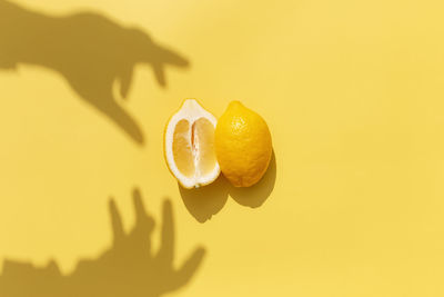 Two halved cuts of lemon with shadow from hand on yellow background. healthy eating, travel