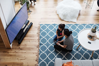 High angle view of mother and daughter watching television while sitting on floor at home