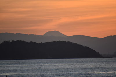 Scenic view of sea and silhouette mountains against orange sky