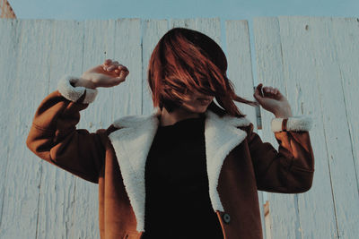 Young woman tossing hair while standing against wall