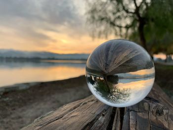 Close-up of crystal ball on lake against sky during sunset