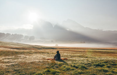 Rear view of man sitting on field against sky