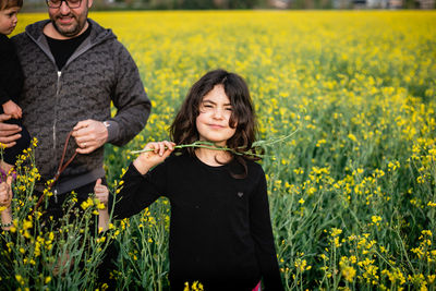 Portrait of a smiling girl standing in front of her father with other siblings amidst yellow flowers