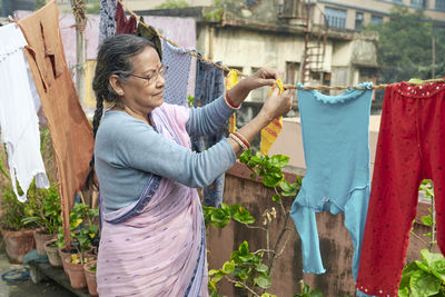 Portrait of a simple looking mature indian woman hanging freshly washed laundry to dry in the sun