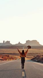 Rear view of woman with arms raised walking on road