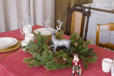 Christmas wreath of fir branches and cones with a statuette of a silver deer on the table, served 