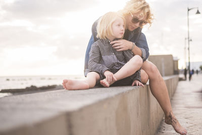 Mother sitting with son on railing against cloudy sky during sunset