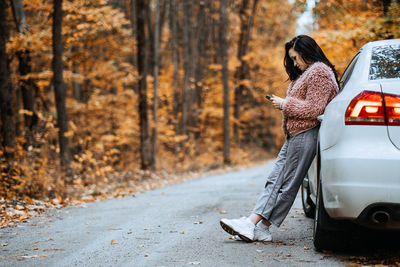Confident brunette woman standing near car and call phone. preparing your car for fall autumn