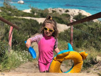 Girl wearing sunglasses while holding inflatable ring and toy at beach