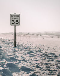 Road sign on snow covered land against clear sky