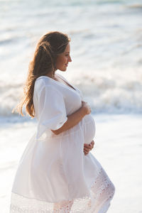 Pregnant woman touching belly standing on beach