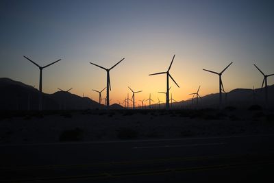 Silhouette wind turbines on field against sky during sunset