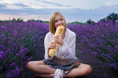 Cute girl eating bread sitting in flower farm