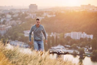 Man playing with dog on field against sky during sunset