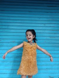 Portrait of a smiling girl standing against blue wall