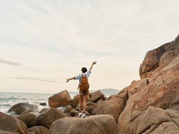 Rear view of woman standing on rock against sky