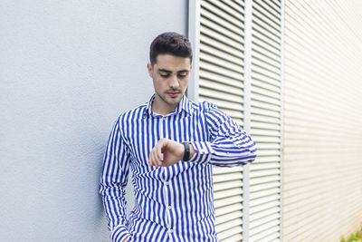 Young man checking the time while standing against wall