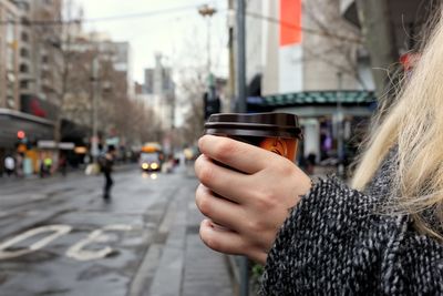 Midsection of woman holding cup of coffee on street