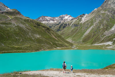 People on mountain by lake against blue sky