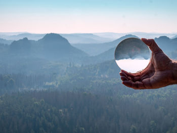 Hand holding mountain range against sky