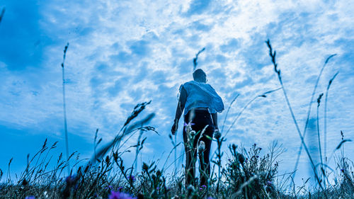 Rear view of woman standing on grass against sky